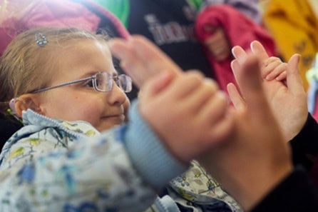 A little girl sitting down holding onto someone's hands
