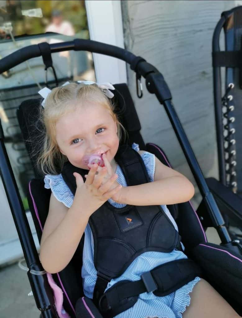 Mia, a young girl with blonde hair, smiling in her wheelchair.
