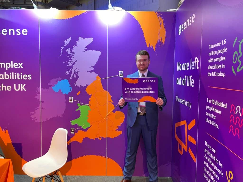 A member of the Sense policy team at our party conference stand with a sign saying "I'm supporting people with complex disabilities".