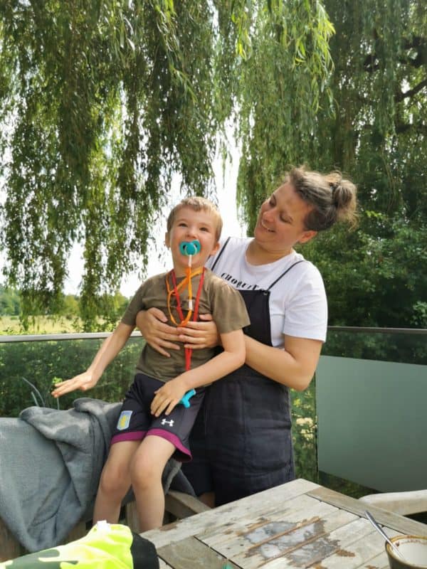 A young boy sits on his mum's lap in a green garden 