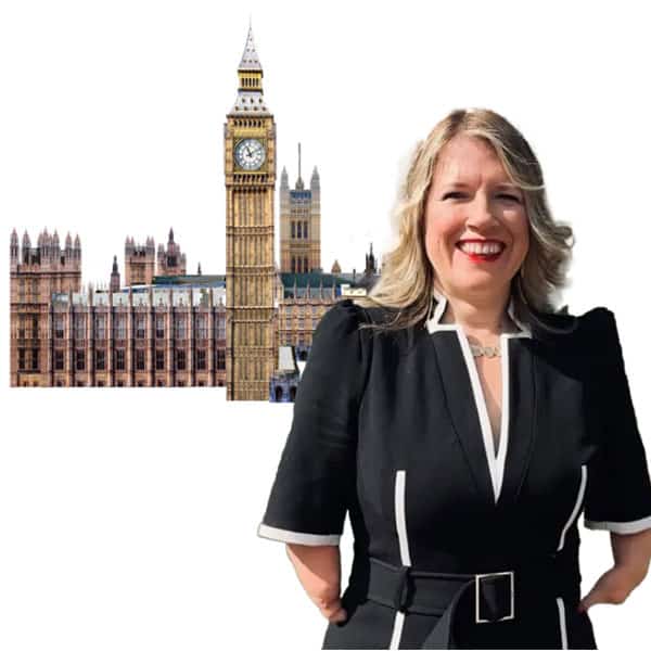 A woman in a suit stands in front of the Houses of Parliament