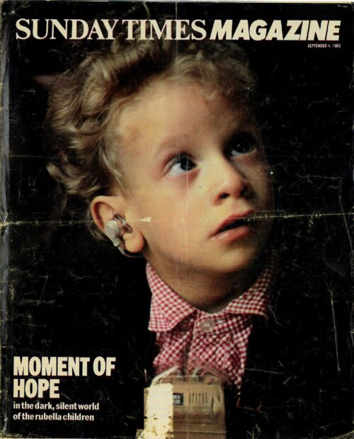 A photograph of a magazine cover for the Sunday Times Magazine. There is a picture of a young boy with curly blonde hair wearing a red and white check shirt and a black jacket. You can see that he is wearing hearing aids. At the bottom of the cover it says "Moment of hope in the dark, silent world of the rubella children."
