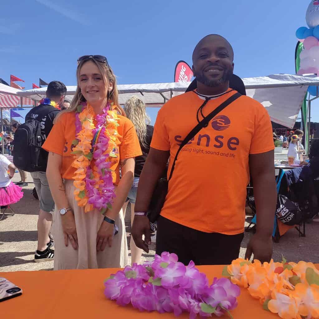 Two people in orange Sense t-shorts smiling at the camera at Birmingham Pride