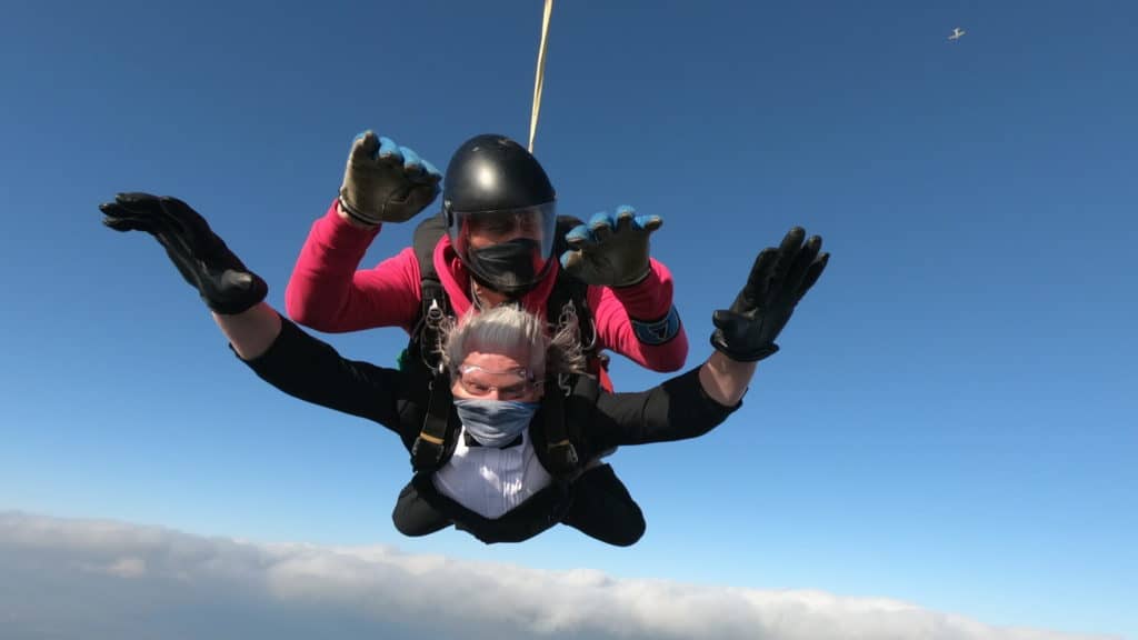 A mid-air shot of two men skydiving in tandem with a blue sky behind them - they look really excited