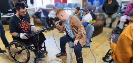 A man plays a synthesiser whist another leans into the microphone singing