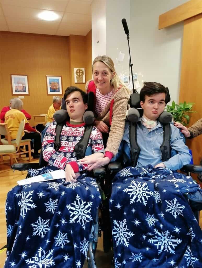 A woman with two teenage boys, both in powered wheelchairs. They have winter themed blankets over their laps.