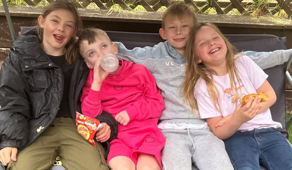 Four children sit on a garden swing seat laughing and smiling