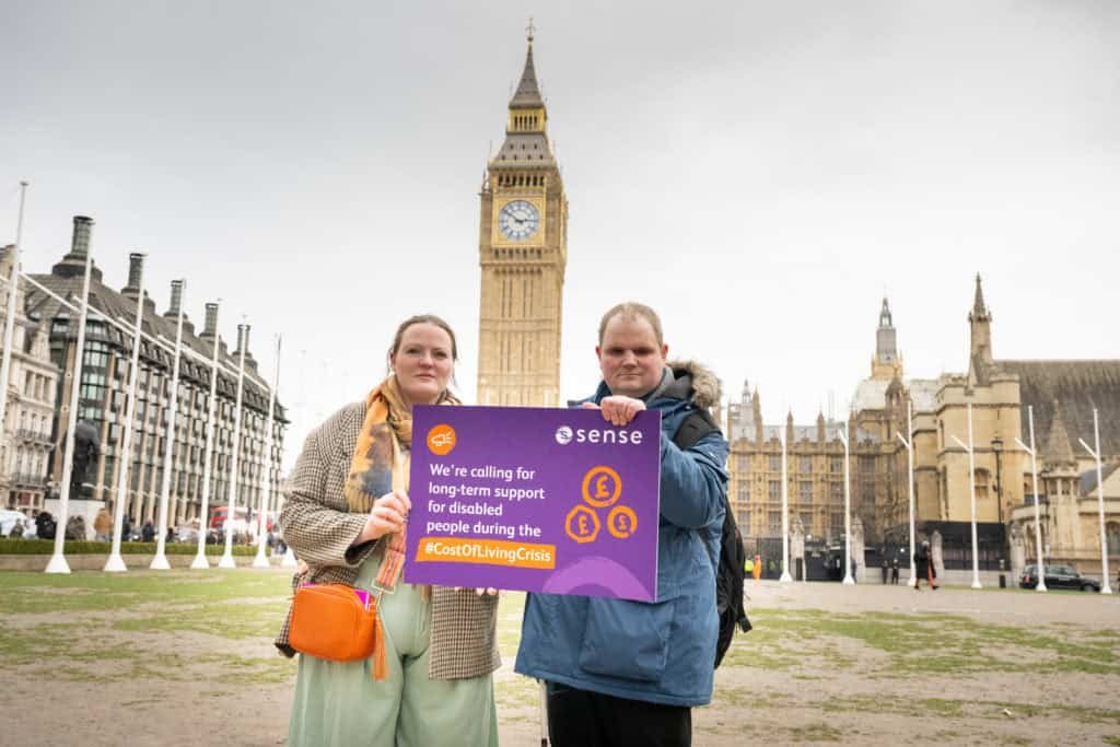 Two people hold up a banner in front of the houses of parliament