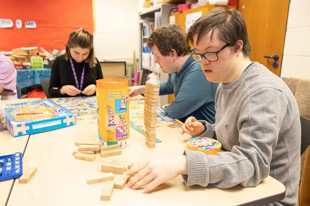 Young people around a table play Jenga and do jigsaws at Sense College.
