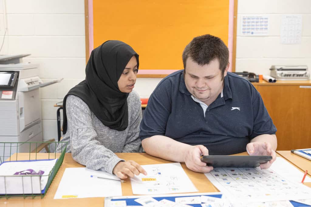 A woman in a hijab points to some paperwork, while a man sat next to her glances over