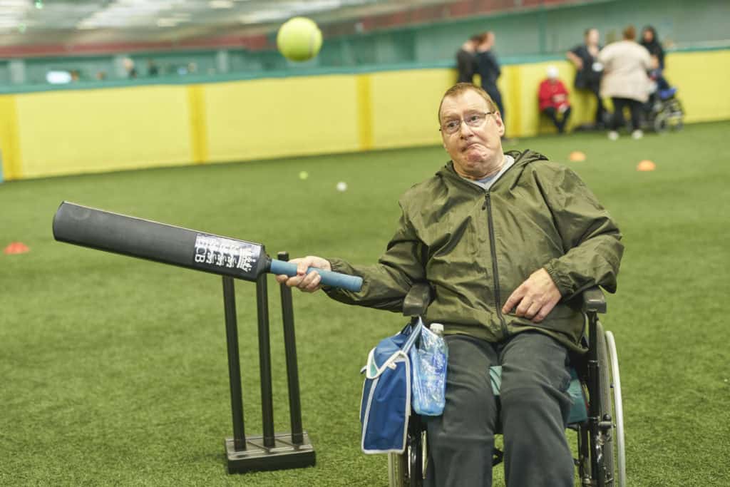 A man playing cricket indoors, hitting a ball that's coming towards him