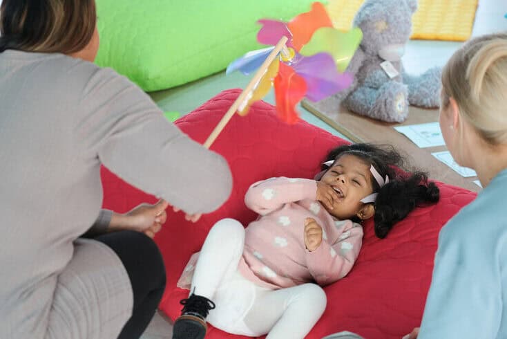 A small girl lies on a cushion, giggling as a wind flag is spun above her.
