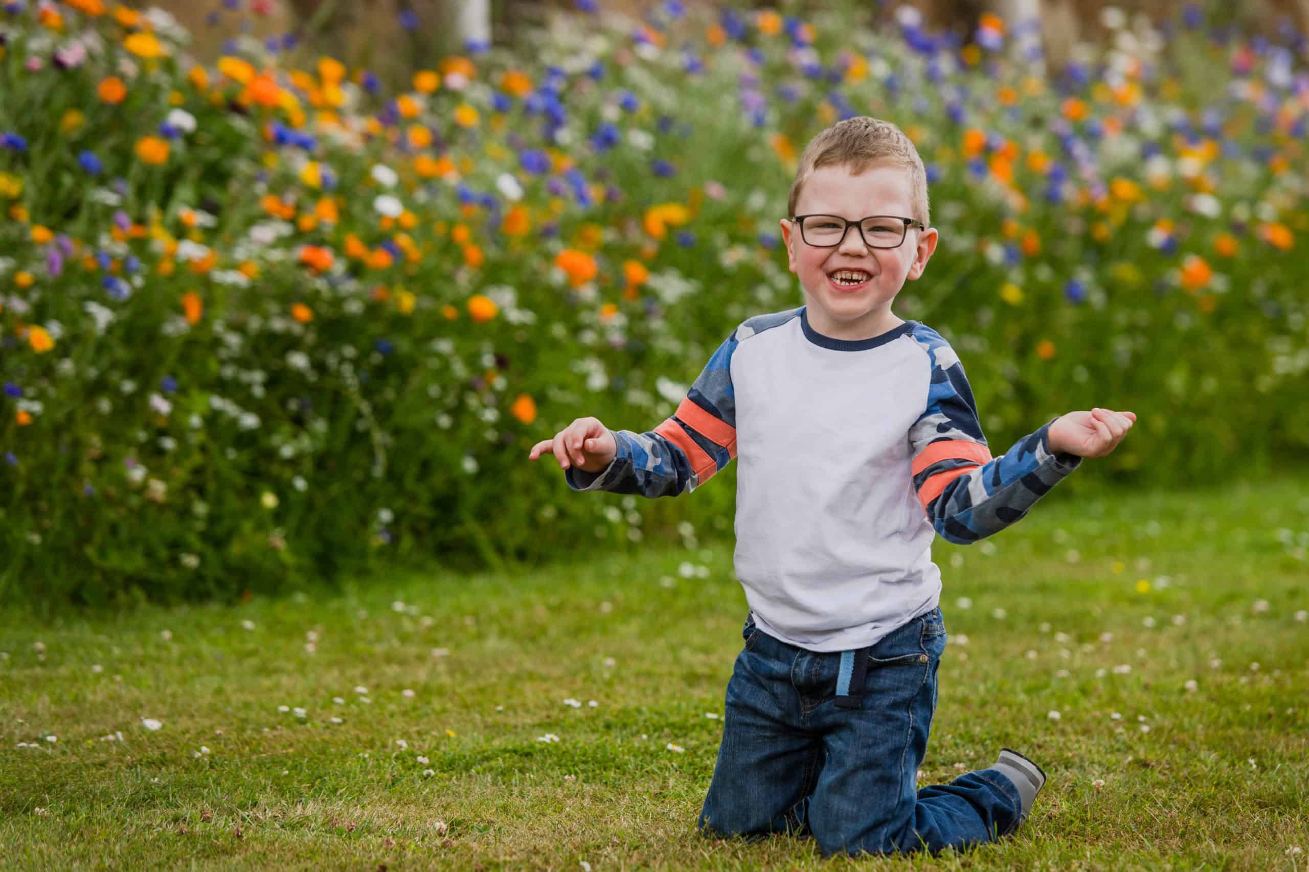 Páuric, a young boy smiling and waving his arms, kneeling on the grass.