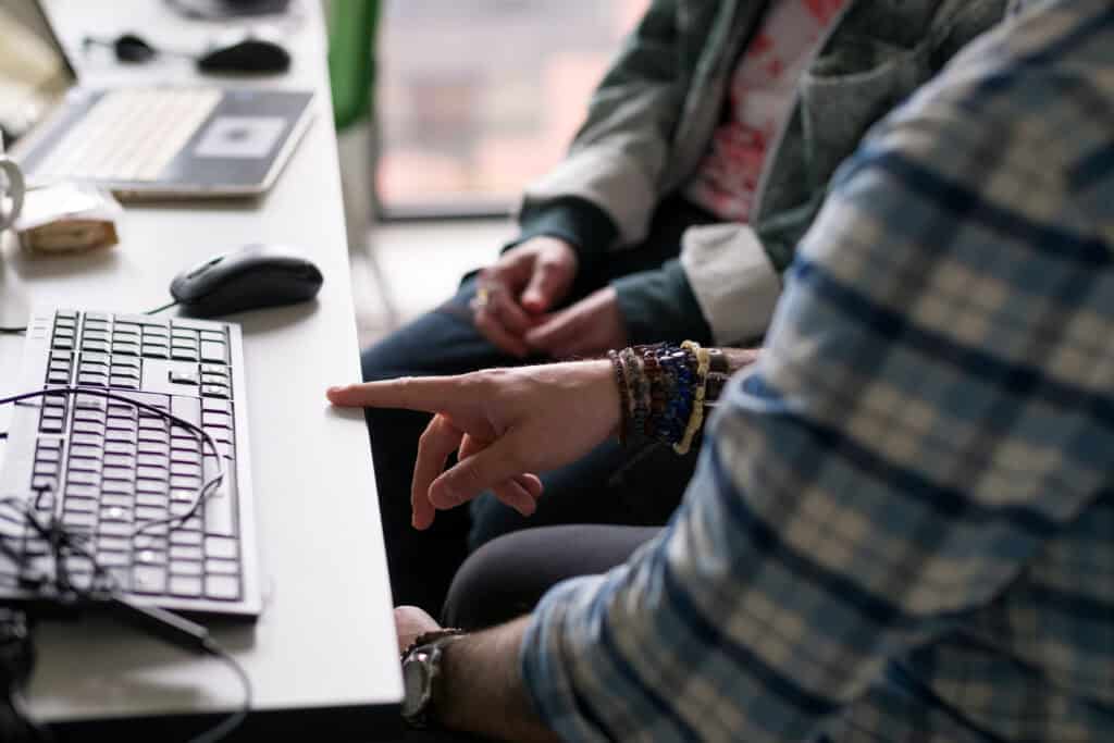 A close-up of two people sitting at a desk, one person is gesturing to the keyboard