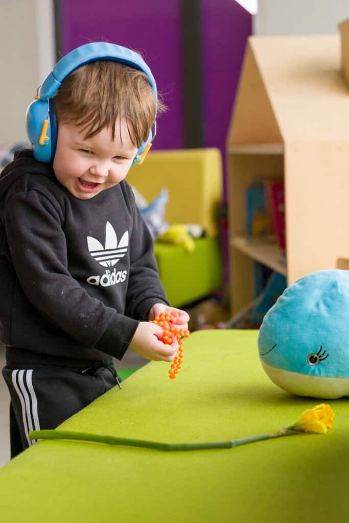 A young boy wearing blue headphones laughing while he plays.