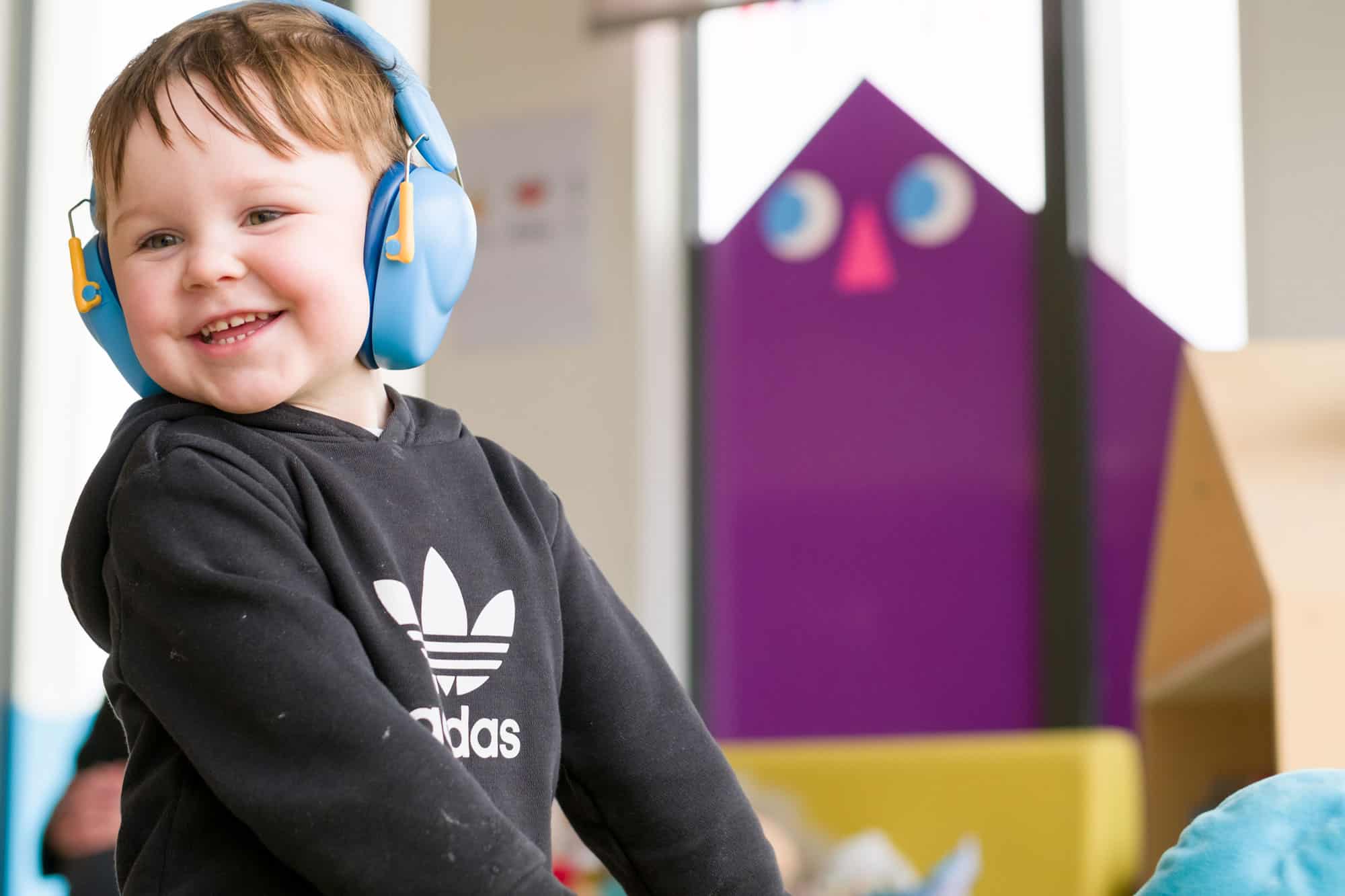 A young child smiling wearing noise cancelling ear muffs