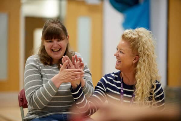 Two women laughing while touching their hands together to communicate.