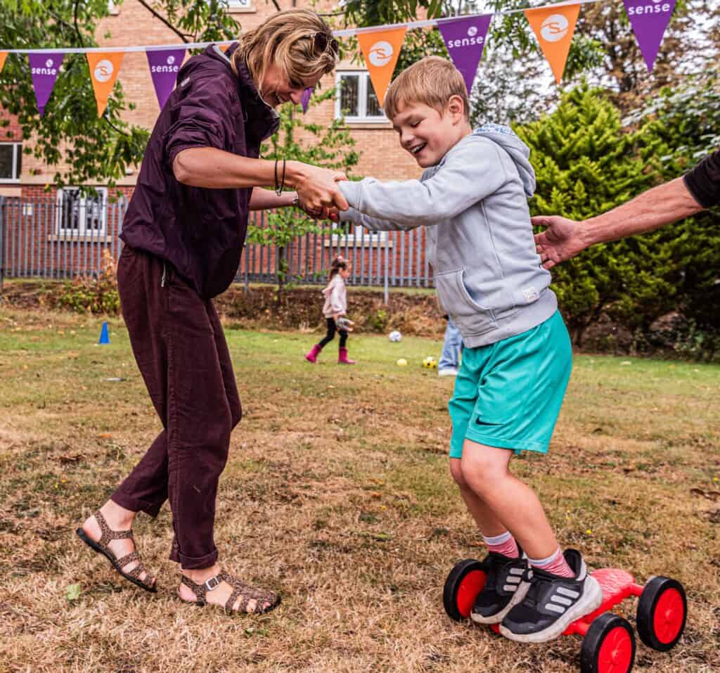 Xander is stood on the pdeal pushers. His mum is holding his hands for support. They are both laughing and looking at the ground trying to balance.