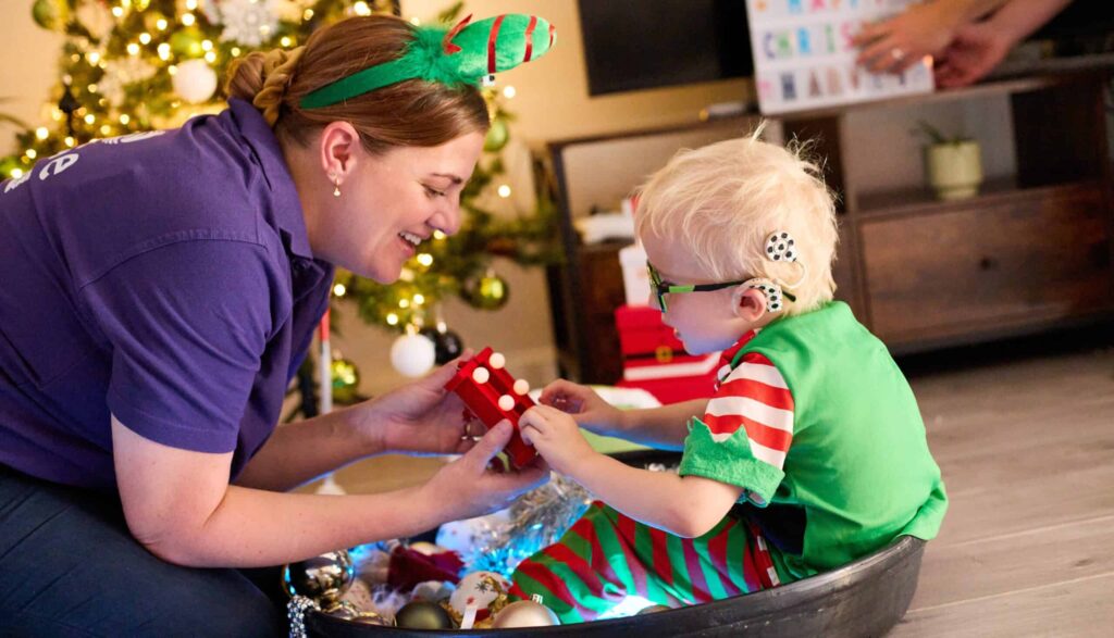 Harvey is sat inside a Messy Play bucket with loads of Christmas items in the area. He is wearing an elf outfit.