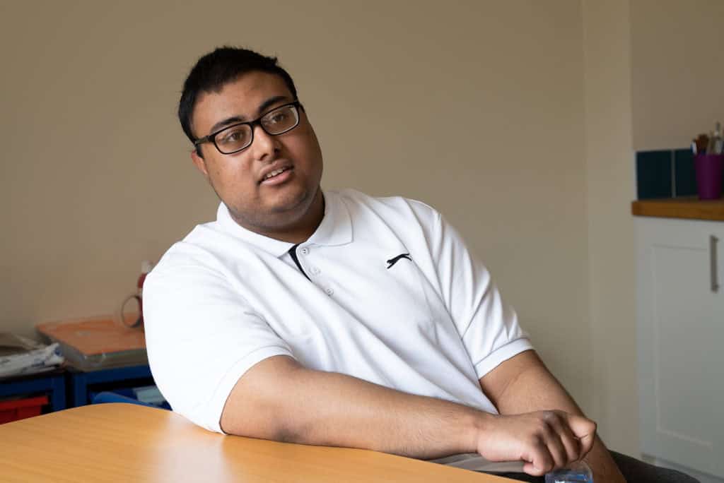A young man in a white poloshirt leaning on a table