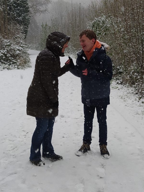 two figures wearing big coats, laughing together in the snow