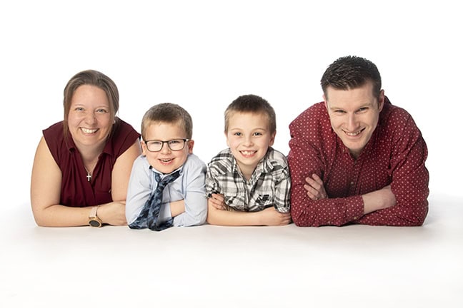 A woman and a man in red shirts and two young boys all lie down with their arms folded, facing the camera and smiling.