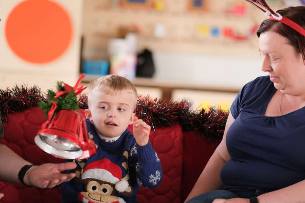 Thomas, a small boy wearing a Christmas jumper, reaches for a shiny red Christmas bell.