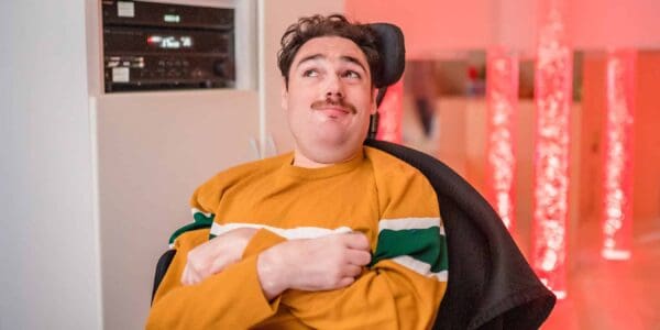 A young man sitting in his wheelchair wearing a yellow top.