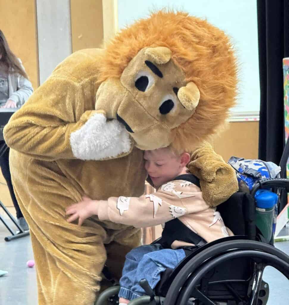 A volunteer in a bear outfit hugging a boy in a wheelchair.