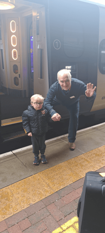 A young boy on a train platform holding hands with a train assistant